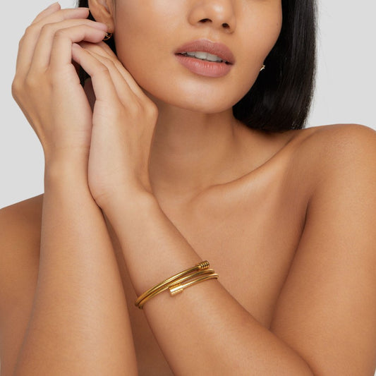 Vrouw draagt het Aurora Luxe armband – stijlvol gedraaid ontwerp in gouden kleur. Een elegant accessoire dat elke look compleet maakt met een moderne, luxueuze uitstraling.