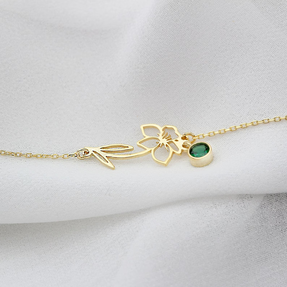 Een delicate gouden Blooming Essence armband met een sierlijke bloemvorm en een groene edelsteenhanger, subtiel gepresenteerd op een zachte witte achtergrond. Deze elegante en persoonlijke armband straalt verfijning uit en is perfect voor liefhebbers van unieke en tijdloze accessoires.