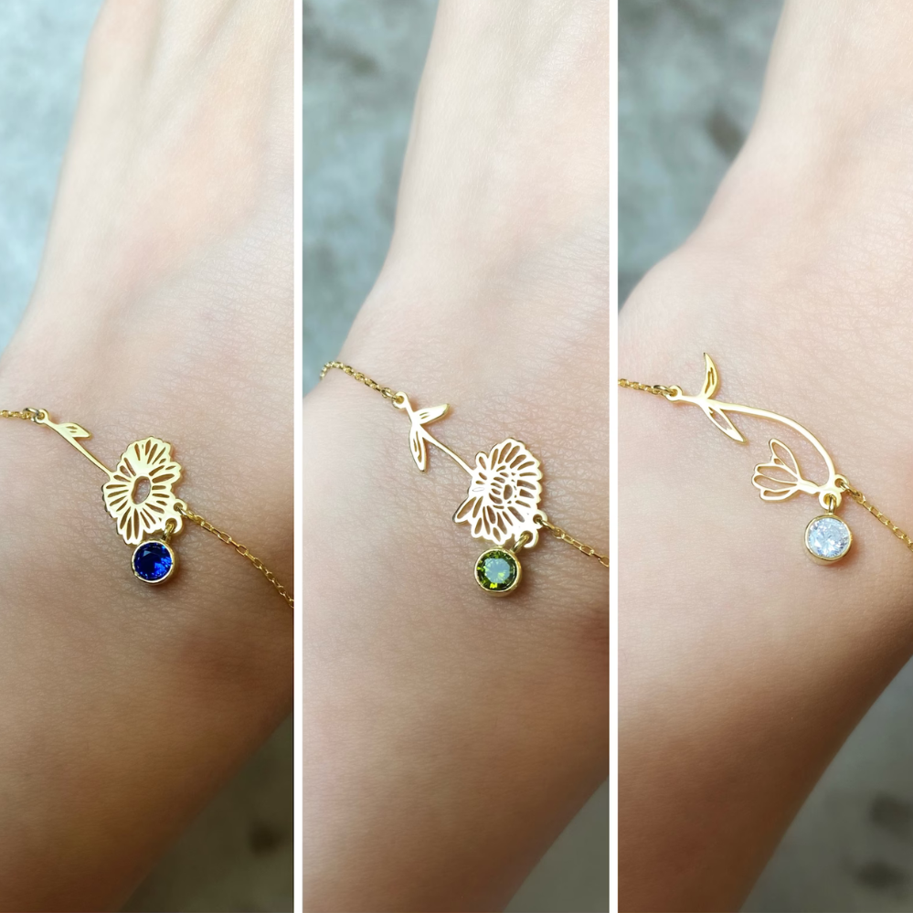 Drie variaties van de elegante Blooming Essence armband, elk met een unieke gouden bloemvorm en een kleurrijke edelsteenhanger in blauw, groen en wit. Deze persoonlijke en stijlvolle armbanden stralen verfijning uit en zijn perfect voor elke gelegenheid.