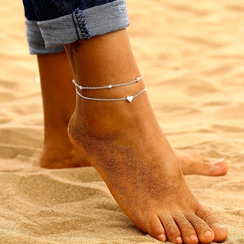 Delicati Charms romantische dubbelgelaagde enkelband, sierlijk ontworpen met hart- en kralendetails, perfect voor een zomerse look op het strand