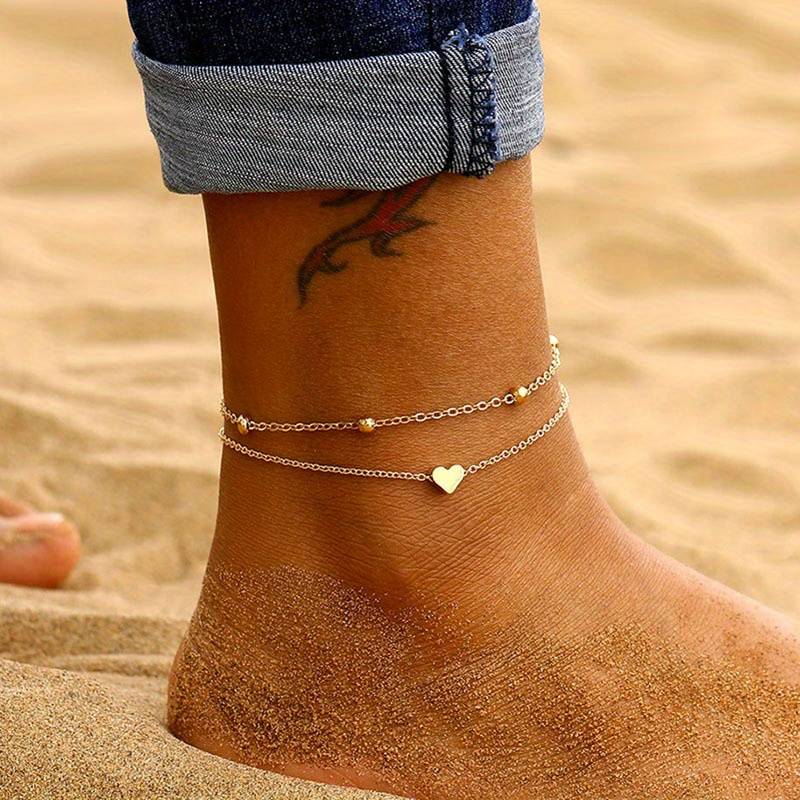 Delicati Charms dubbelgelaagde enkelband met hart- en kralendetails, een romantisch sieraad voor zomerse dagen op het strand.