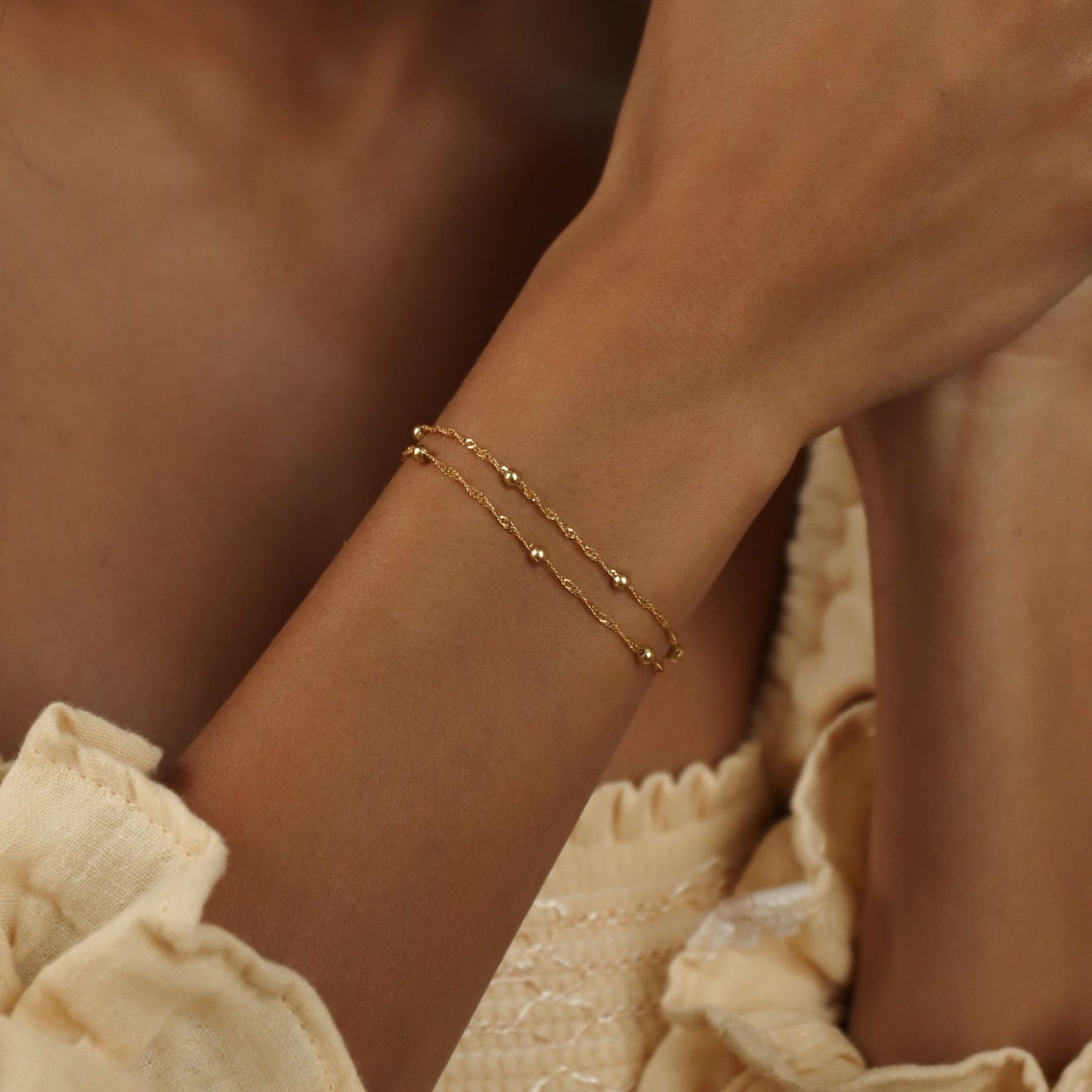 Een elegante close-up van een pols met een minimalistische gouden AstroChic Sterrenarmband, bestaande uit twee fijne kettingen met subtiele bolvormige accenten. Deze verstelbare en stijlvolle armband straalt eenvoud en verfijning uit, perfect als persoonlijk accessoire voor een tijdloze look.