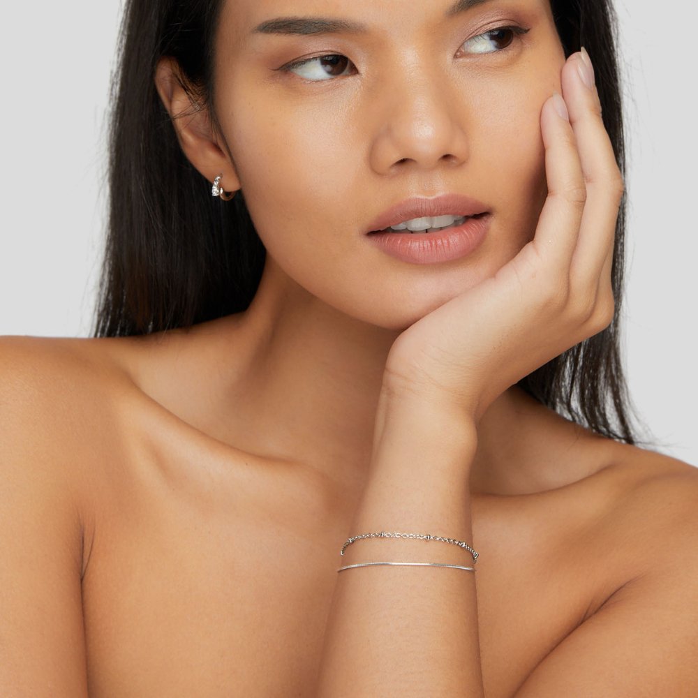 Vrouw draagt het Lumen Luxe multilagen armband – elegante en verfijnde zilverkleurige armbanden, minimalistisch en stijlvol. Perfect accessoire voor een subtiele, luxueuze uitstraling.