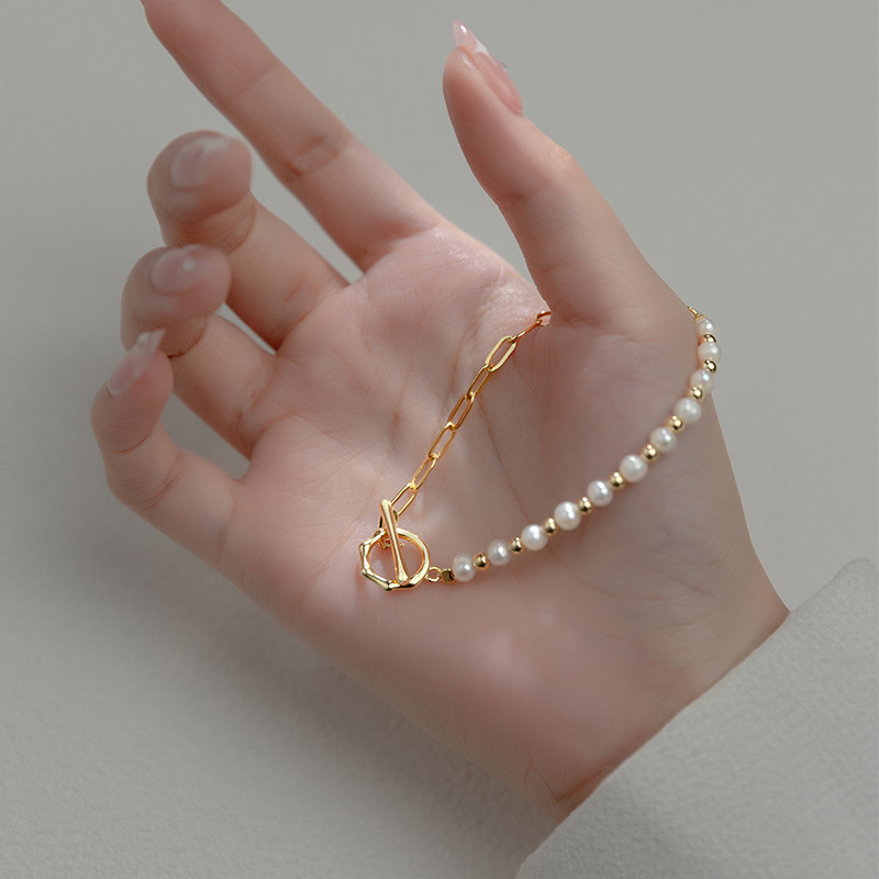 Delicate Lumina Grace parel schakelarmband met een verfijnde combinatie van glanzende parels en gouden schakels, weergegeven in een hand. Een tijdloze luxe accessoire die elegantie toevoegt aan elke outfit. Perfect voor zowel dagelijks gebruik als speciale gelegenheden.