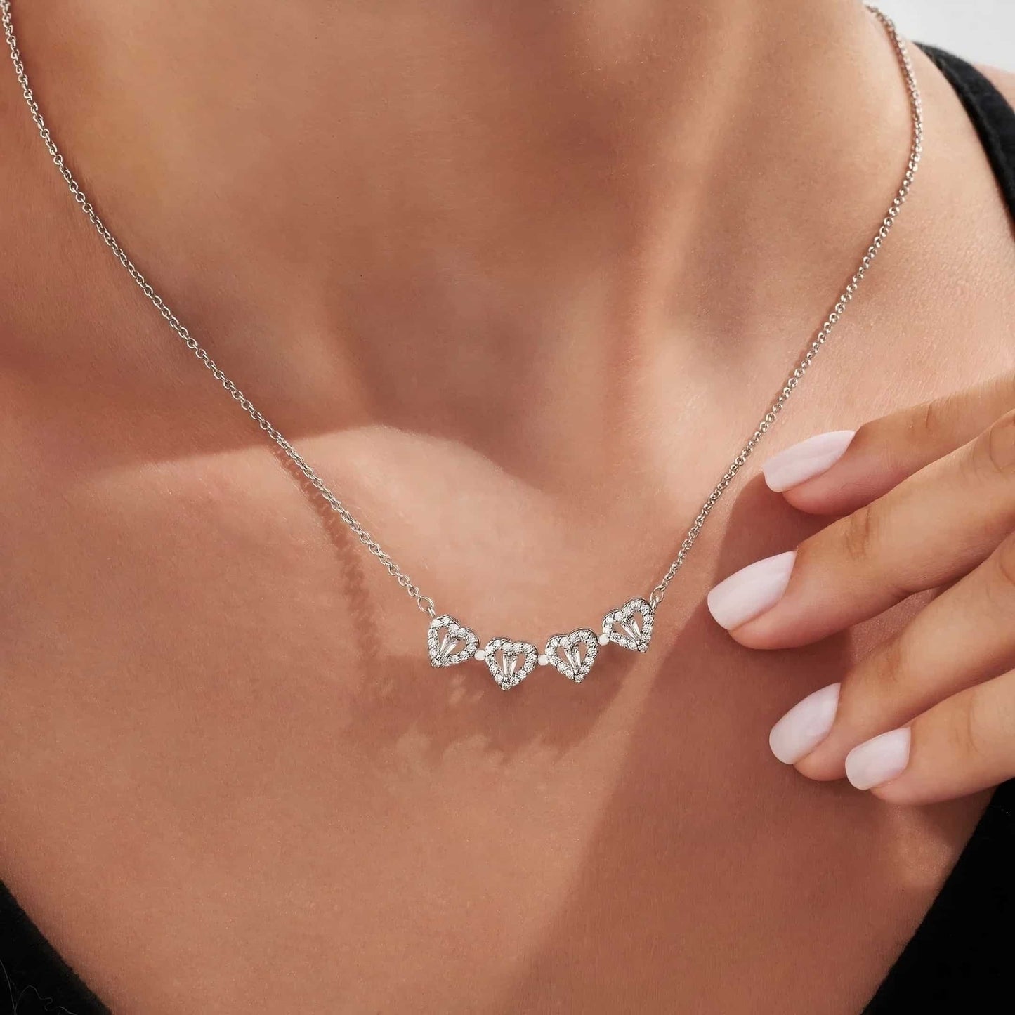 Een elegante vrouw draagt de Luminous Charm zilveren hartketting met meerdere verfijnde hartvormige hangers. De sprankelende details van de Luminous Charm ketting stralen tijdloze elegantie uit en voegen een vleugje luxe toe aan elke outfit."