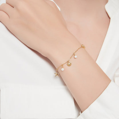 De Lustrous Joy armband is een charmant en stijlvol verfijnd accessoire, versierd met delicate parels en sierlijke schelpen- en stervormige bedels. Het gouden kettingontwerp voegt een elegante glans toe, perfect voor elke gelegenheid. Dit armbandje is een perfecte manier om subtiele luxe te dragen, met een maritiem geïnspireerde uitstraling die bij elke stijl past.