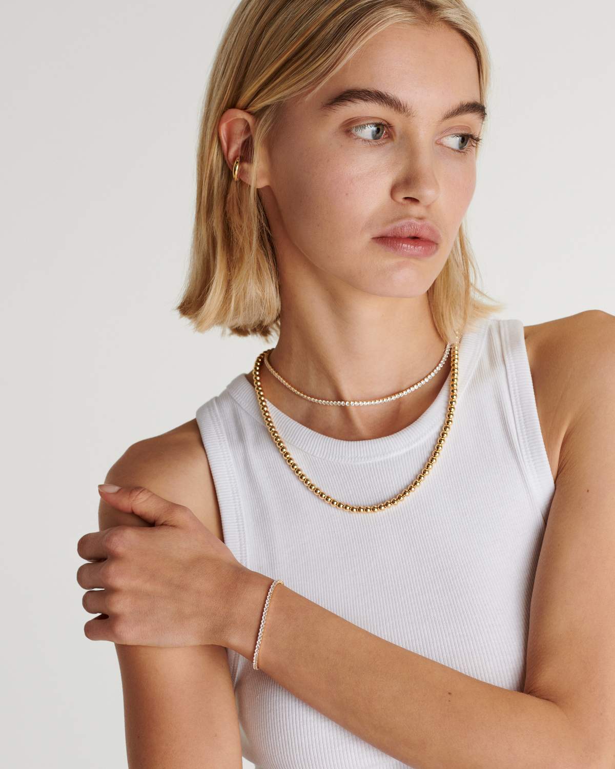 Sterrenlicht Chic tennisarmband met een verfijnd design, gedragen met een elegante witte top. Het iconische, tijdloze ontwerp van de armband past perfect bij de luxe uitstraling van de model, en biedt een subtiele, maar verfijnde aanvulling op elke look