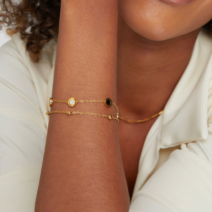 Vrouw draagt het UniekAura armband – een verfijnd ontwerp met gouden dubbele ketting en sierlijke ronde details. Stijlvol accessoire dat elke outfit verrijkt met een elegante en unieke uitstraling