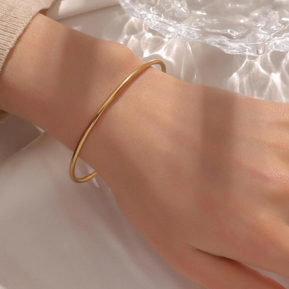 Een delicate gouden armband van Zenith Glamour, elegant om een pols gedragen. De gladde, minimalistische afwerking straalt tijdloze stijl uit, perfect voor het subtiel accentueren van elke look. Een ideale keuze voor een verfijnd en persoonlijk statement.