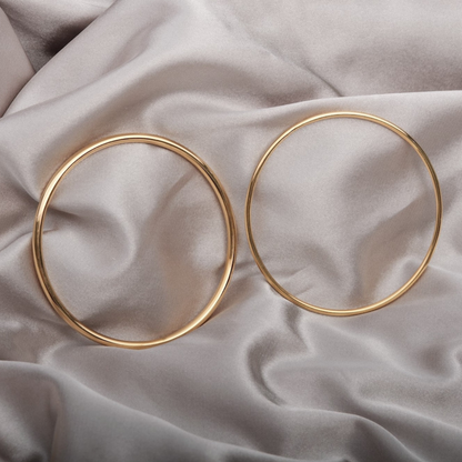 Twee minimalistische gouden armbanden van Zenith Glamour, elegant gepresenteerd op een zachte, glanzende stof. Het tijdloze ontwerp straalt verfijning uit en vormt een perfect accessoire voor elke gelegenheid. Ideaal als cadeau of voor een persoonlijk accent.