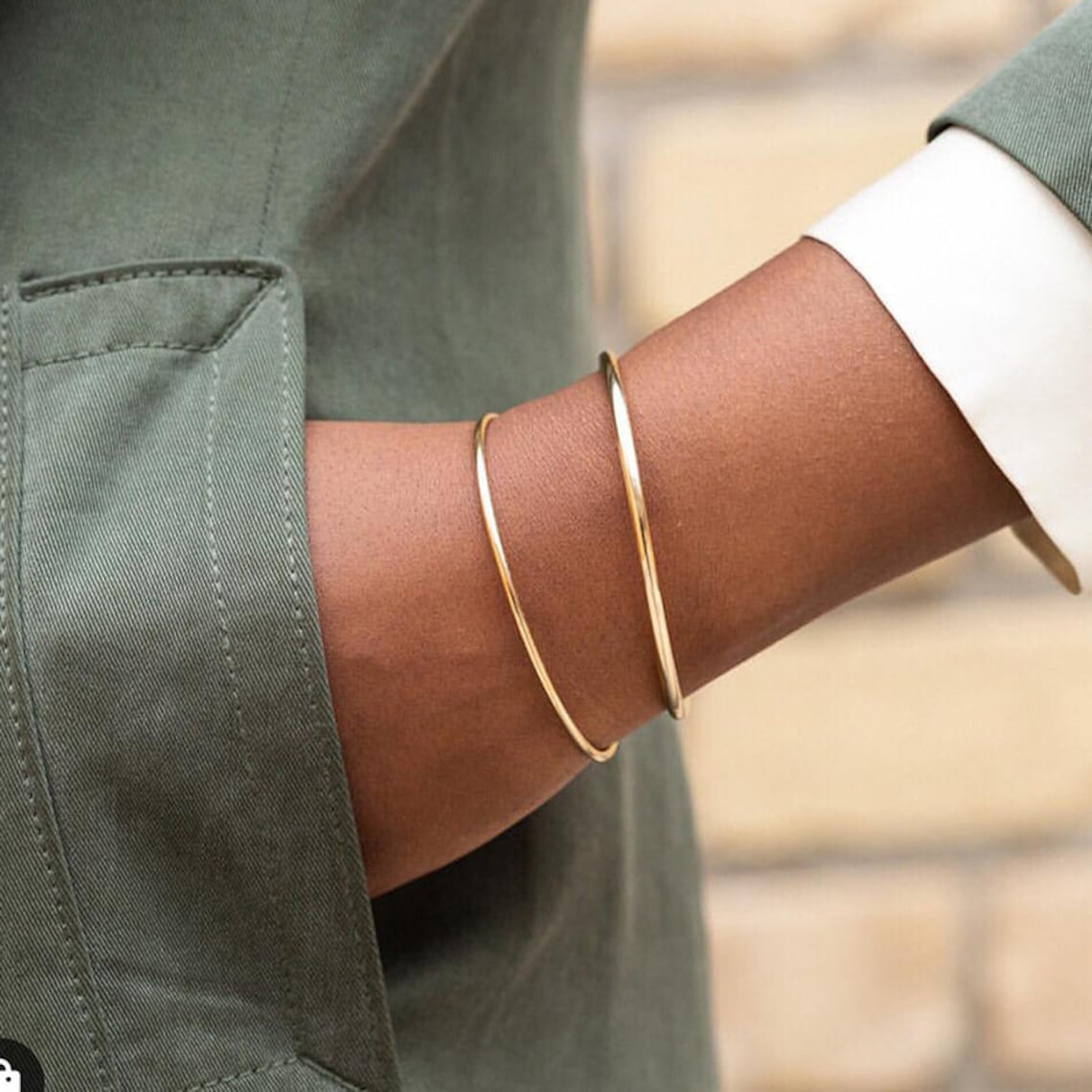 Een stijlvolle close-up van een pols gehuld in twee elegante gouden Zenith Glamour armbanden. Deze minimalistische en verfijnde accessoires voegen een vleugje tijdloze glamour toe aan elke outfit en zijn perfect voor zowel dagelijkse als formele gelegenheden.